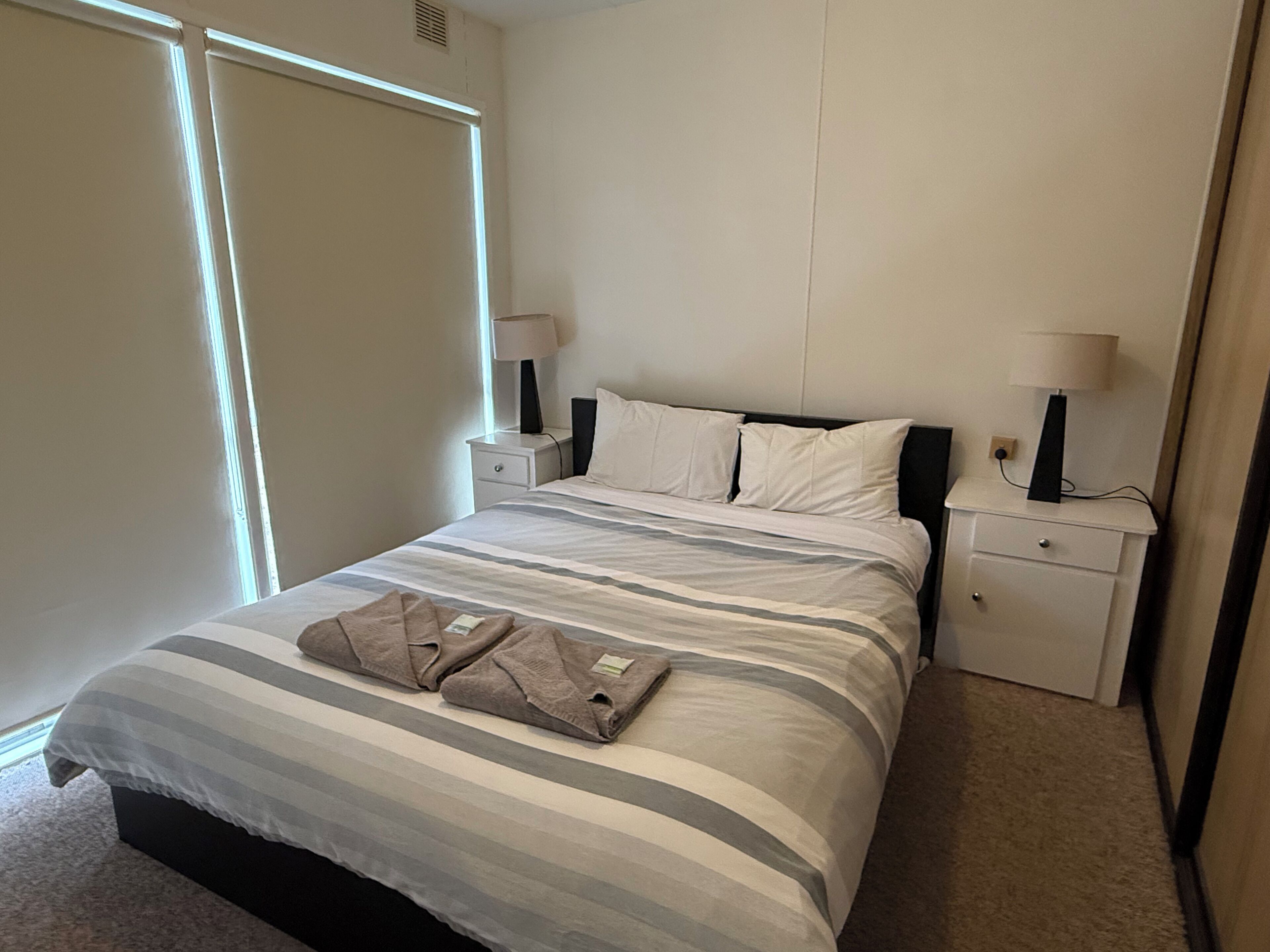 Ein Hotelzimmer mit einem Bett, zwei Nachttischen, zwei Lampen, einem Fenster und einer Tür.