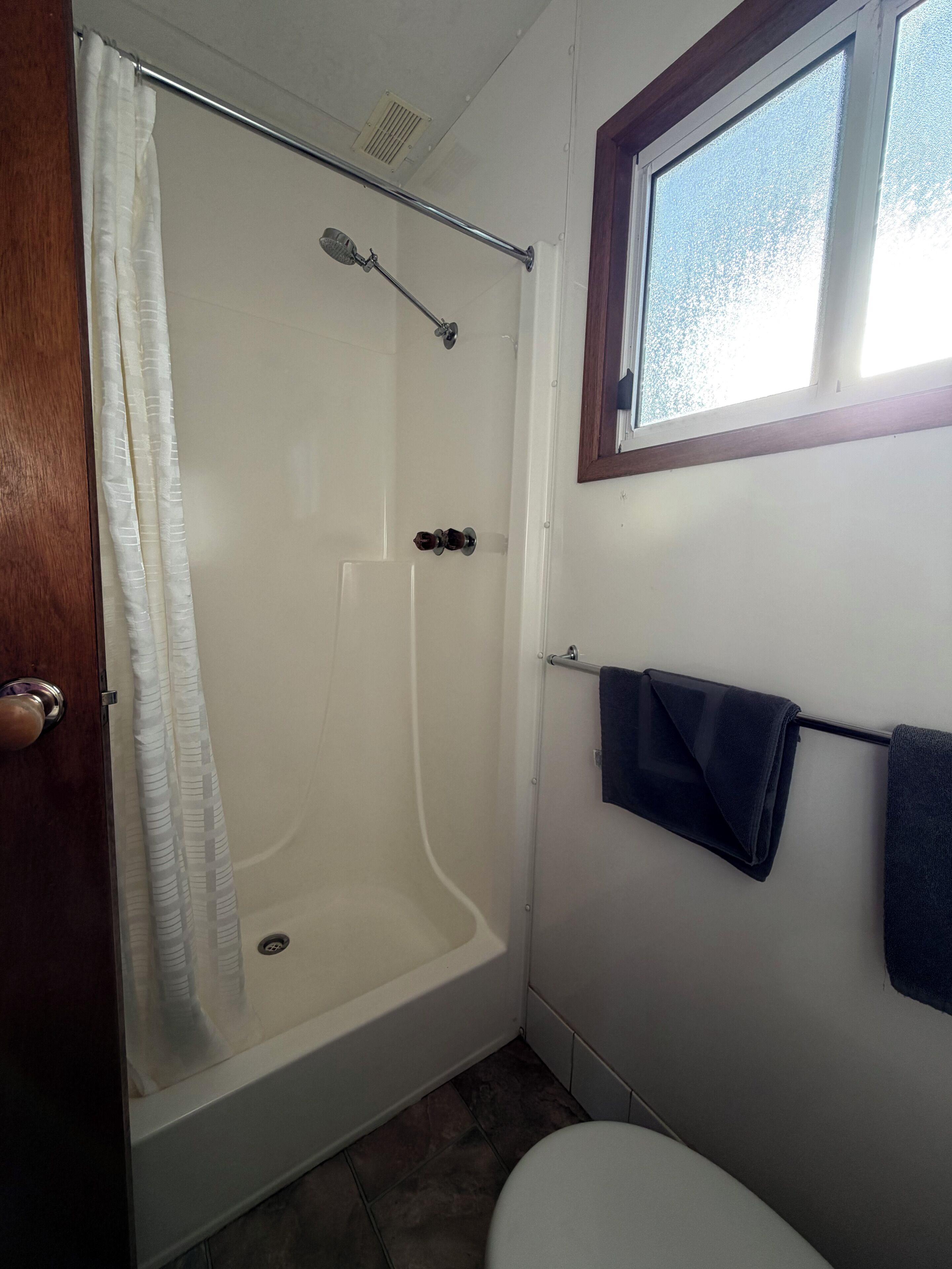 A bathroom with a shower, a toilet, a towel rack, and a window.