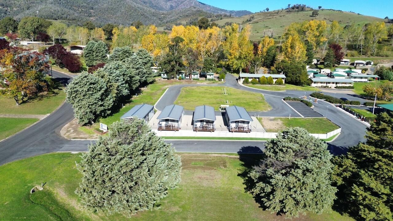 A campground with RVs parked in rows, surrounded by trees and a hilly landscape.