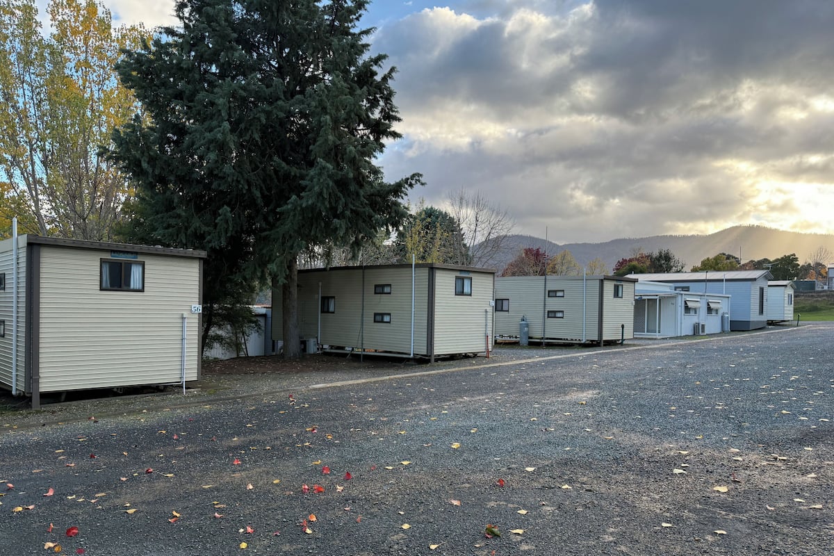 A row of mobile homes with a gravel driveway and trees in the background.