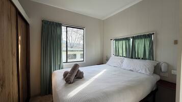 A bedroom with a bed, a window with curtains, a bedside table, and a wooden wardrobe.
