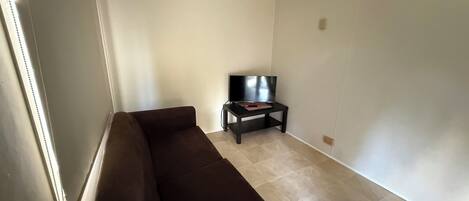 A living room with a brown sofa, a television on a stand, and a tiled floor.