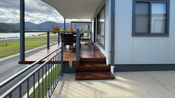 A covered outdoor area with a wooden deck, a metal railing, and a view of a lake and mountains. - Tiny Away Escape at Talbingo Alpine (Talbingo)