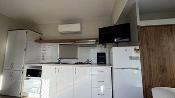 A compact kitchen with white cabinetry, a built-in microwave, a gas stove, a refrigerator, and a flat-screen TV mounted above the stove.