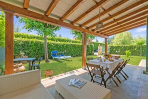 A covered patio with a table set for dining, outdoor seating, and a view of a well-maintained garden. - Casa Colombo with Garden In Forte Dei Marmi, Forte dei Marmi, Italy (Forte dei Marmi)