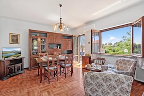 A dining area with wooden furniture, a television, and a view of greenery outside. - Casa Colombo with Garden In Forte Dei Marmi, Forte dei Marmi, Italy (Forte dei Marmi)