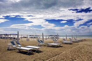 Ein Strand mit Liegestühlen und Sonnenschirmen, einem klaren Himmel und dem Meer im Hintergrund.