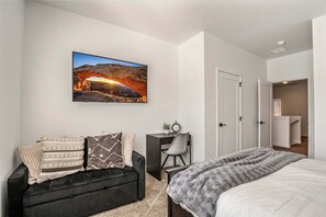 A bedroom with a bed, a black sofa with patterned cushions, a desk with a chair, a painting of a canyon, and a door leading to a bathroom. - Skyline 1729, Golf Simulator, Oversized Hot Tub, and Resort Amenities (Washington)