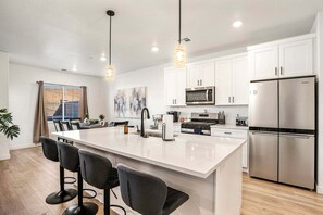 A modern kitchen with white cabinets, a central island with bar stools, stainless steel appliances, and pendant lighting. - Skyline 1729, Golf Simulator, Oversized Hot Tub, and Resort Amenities (Washington)