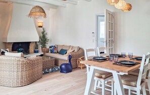 A cozy living area with a sofa, wicker furniture, a dining table set for four, and a fireplace. - Amazing home in Le Pouliguen with WiFi (Le Pouliguen)