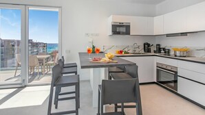 Una cocina moderna con una isla central, un comedor con sillas y vistas al mar a través de amplios ventanales.