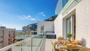 Un balcón con mobiliario para comer, un jacuzzi y vistas al mar y edificios.