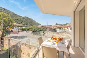 Ein Balkon mit Frühstückstisch, der auf eine gebirgige Landschaft mit Gebäuden blickt.