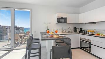 Una cucina moderna con isola centrale, zona pranzo con sedie e vista sul mare attraverso ampie finestre.