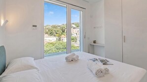 Een hotelkamer met een groot raam, een bed met witte lakens, een nachtkastje en een kledingkast.
