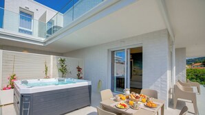 Een modern terras buiten met een hottub, eettafel, stoelen en uitzicht op een woongebouw.