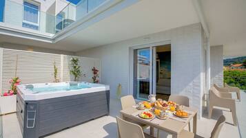 Eine moderne Außenpatio mit Whirlpool, Esstisch, Stühlen und Blick auf ein Wohngebäude.