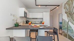 Een moderne keuken met witte kasten, een marmeren achterwand en een eethoek met een donker aanrecht en stoelen.