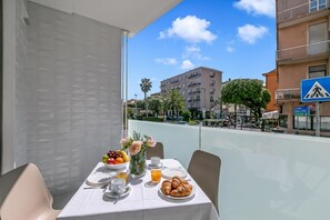 A balcony with a table set for breakfast, including croissants, fruit, and juice, overlooking a cityscape with buildings and palm trees. - Nua Boutique Apartaments 16 Towncentre, Finale Ligure, Italy (Finale Ligure)