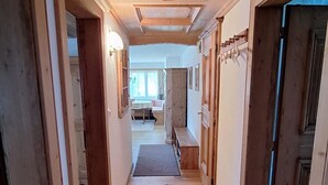 Un corridoio in legno con una panca, una porta e vista su una stanza con tavolo e sedie.