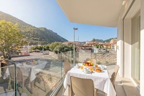 Ein Balkon mit Frühstückstisch, Glasgeländer und Blick auf eine Hügelstadt.