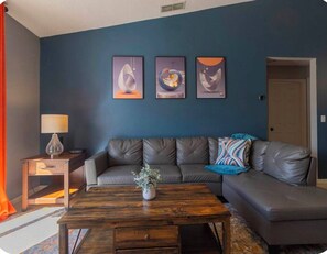 Ein Wohnzimmer mit einer Couch, einem Couchtisch, einer Lampe und drei gerahmten Kunstwerken an der Wand.