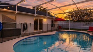 Une piscine avec un patio couvert, un parasol rouge et une vue sur le coucher de soleil.