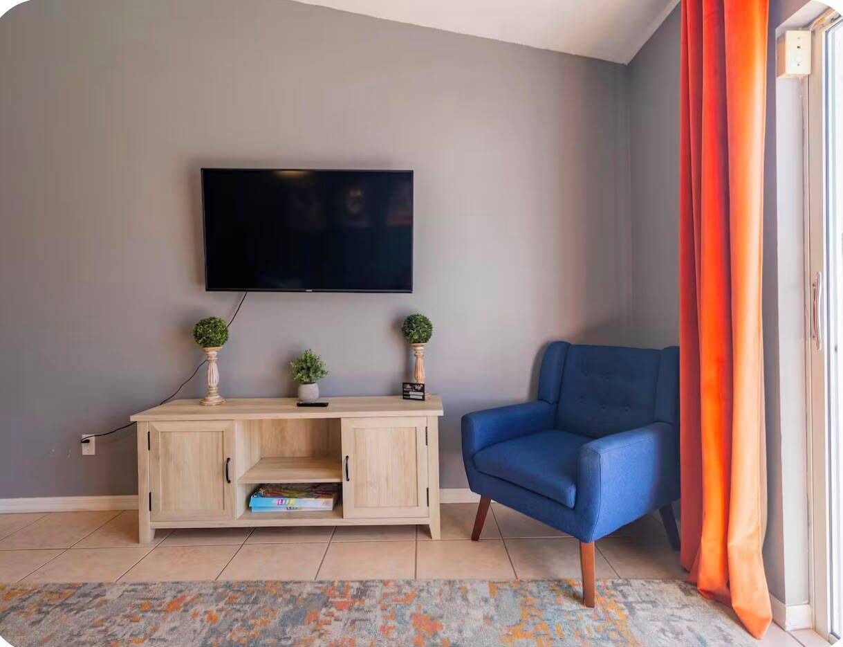 A living room with a TV mounted on the wall, a blue sofa, a wooden cabinet with decorative items, and a patterned rug.