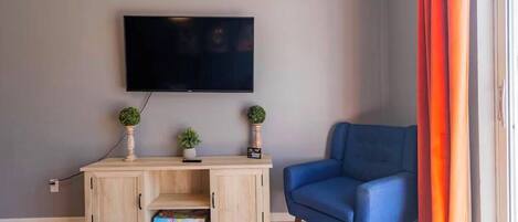A living room with a TV mounted on the wall, a blue sofa, a wooden cabinet with decorative items, and a patterned rug.
