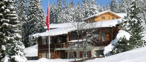 A wooden lodge with a red flag, surrounded by snow-covered trees.
