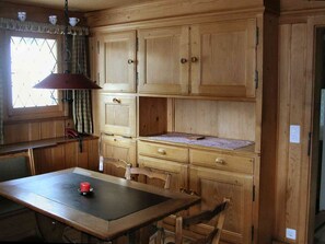 A wooden kitchen with a table, chairs, and a hanging light fixture. - Guarda Cuolms Schütz Appartement/Fewo,   Guarda Cuolms Schütz by Interhome (Lenzerheide)