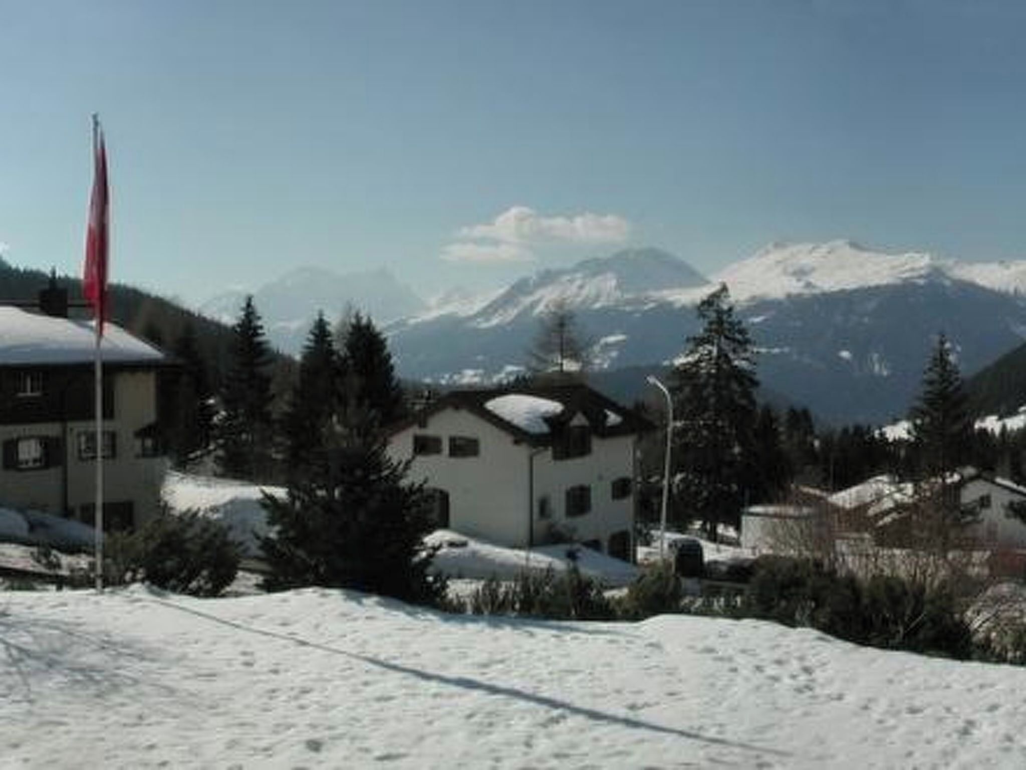 A building with a snow-covered roof, surrounded by trees and mountains in the background.