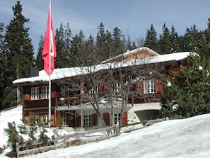 Eine Holzhütte mit einer roten Fahne, umgeben von Schnee und Bäumen.