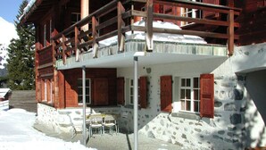 A chalet with a stone facade, wooden balcony, and a patio area with outdoor furniture.