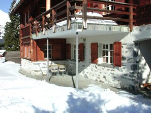 Eine Chalet mit Steinaußenwand, Holzbalkon und einer Terrasse mit Gartenmöbeln.
