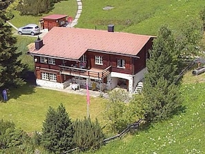 Ein zweistöckiges Holzhaus mit rotem Dach, einem Balkon und einem gepflasterten Einfahrt.