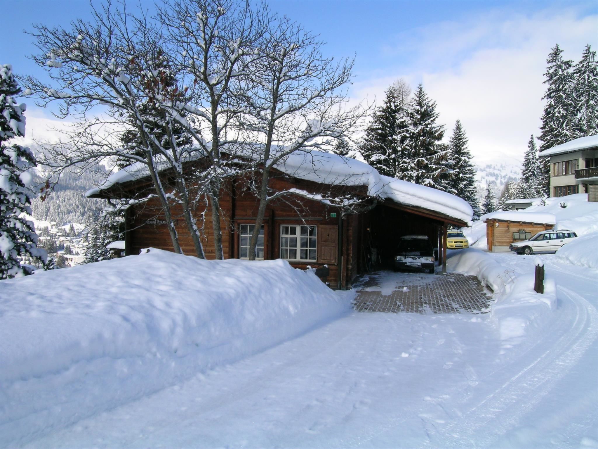 A wooden cabin with a covered entrance, surrounded by snow-covered trees and a clear sky.