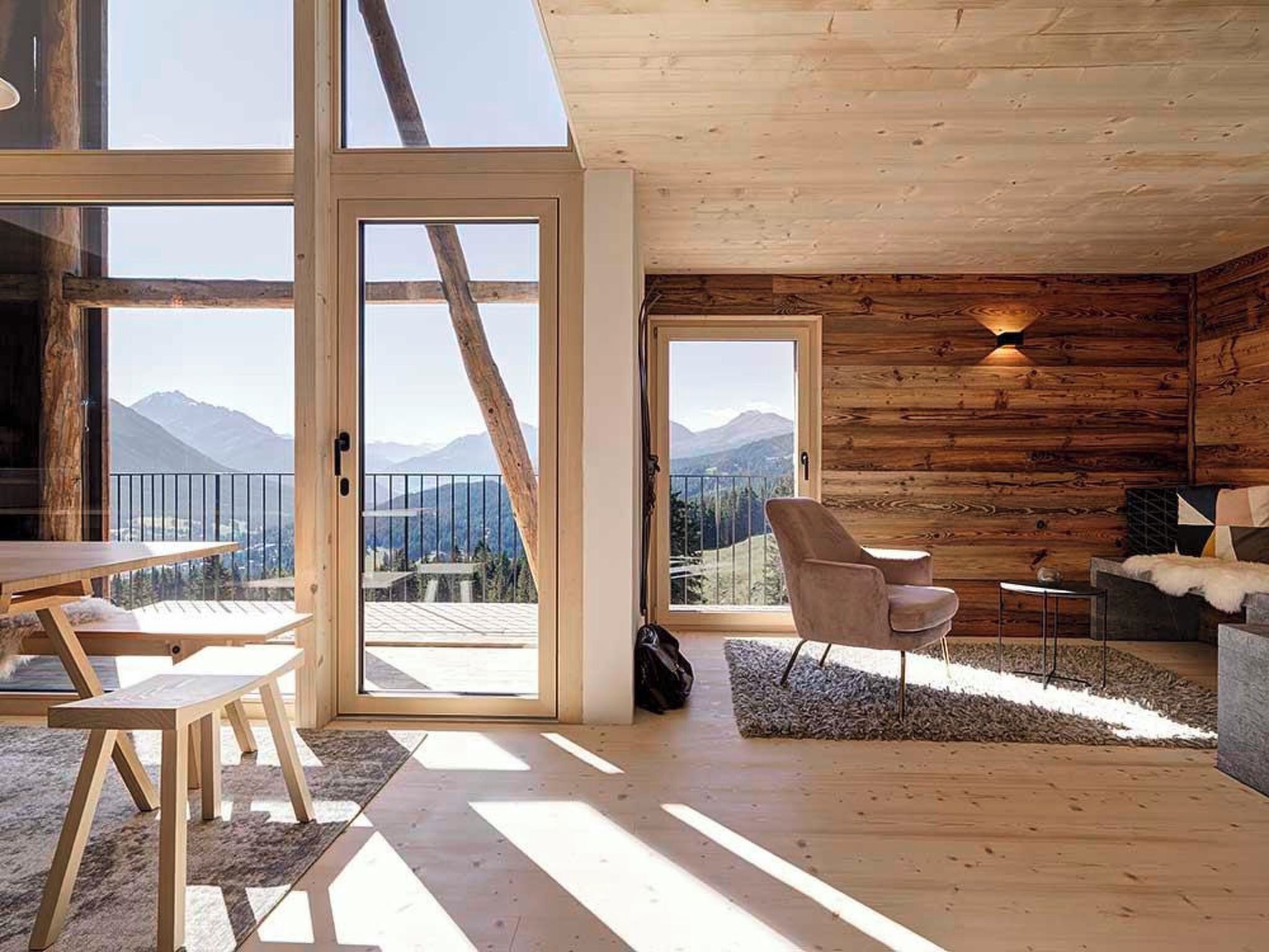 A wooden cabin with large sliding glass doors leading to a balcony with a mountain view.