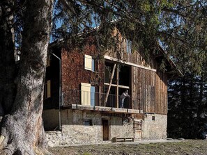 A rustic wooden building with a balcony, a stone foundation, and a large tree in the foreground. - Alphütte Briula Appartement/Fewo, Dusche, WC, 3 Schlafräume by Interhome (Valbella)