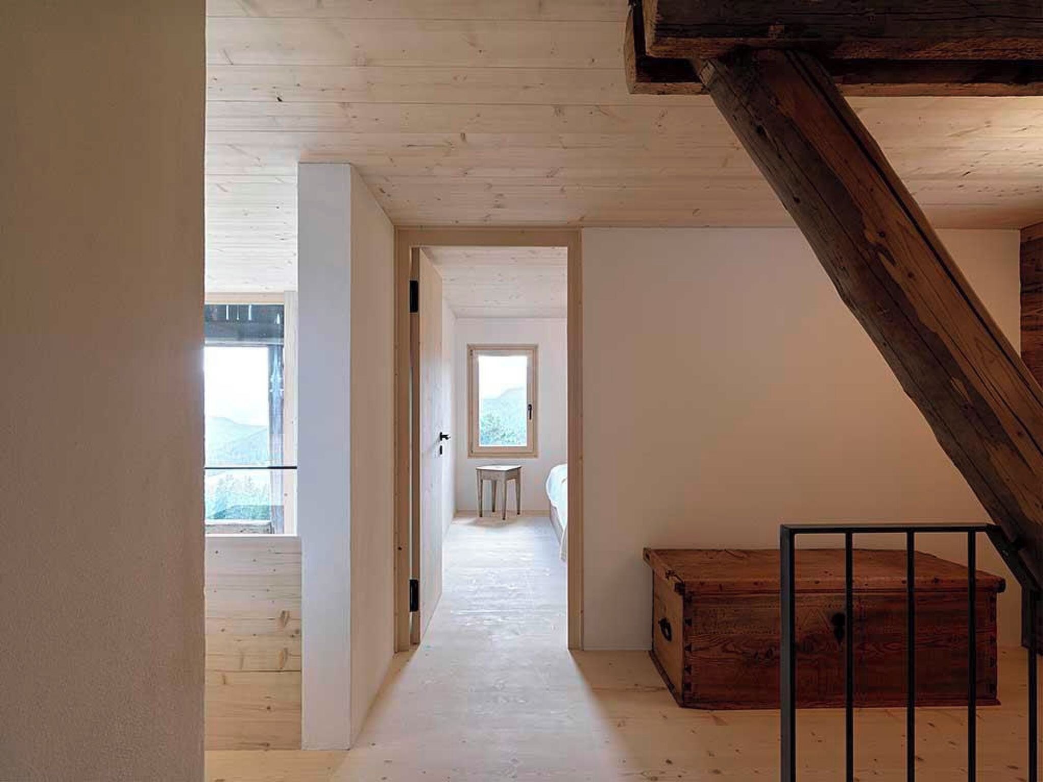 A narrow hallway with wooden flooring, a staircase on the right, and a window at the end.