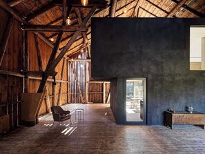 Un interior espacioso con vigas de madera, una pared oscura y una vista a través de una puerta.