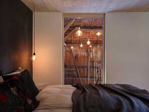 A bedroom with a bed, a wooden ladder, and hanging light fixtures.