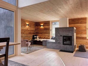A modern interior with wooden walls, a stone fireplace, and a seating area with a sofa and chairs. - Alphütte Briula Appartement/Fewo, Dusche, WC, 3 Schlafräume by Interhome (Valbella)