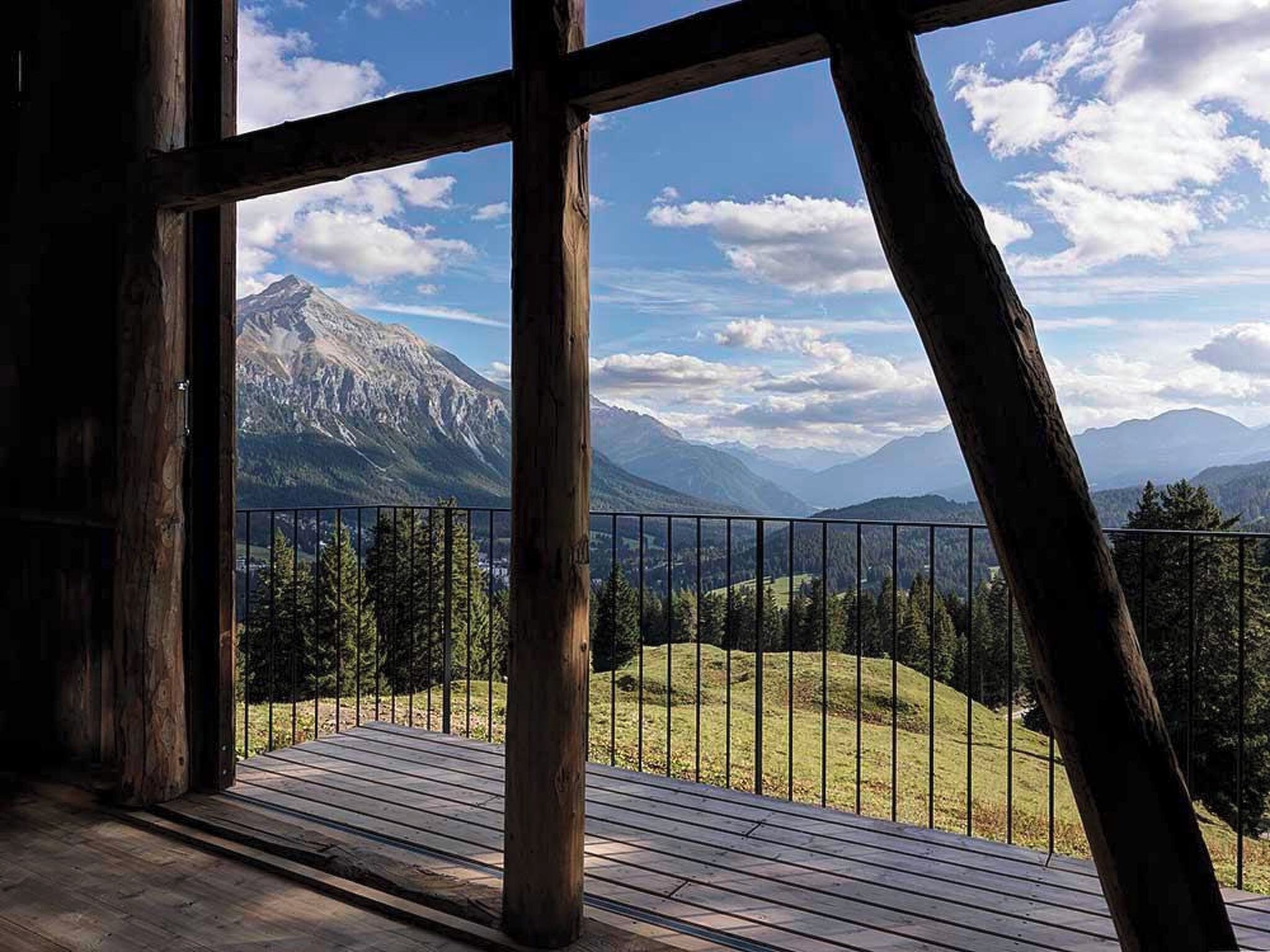 Une terrasse en bois offrant une vue sur les montagnes, avec une rambarde en métal et un ciel dégagé.