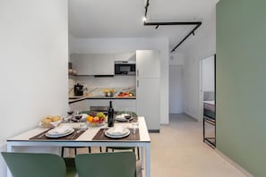 A modern kitchen with white cabinets, a dining table set with plates, glasses, and a fruit bowl. - Nua Boutique Apartaments 13 Towncentre, Finale Ligure, Italy (Finale Ligure)