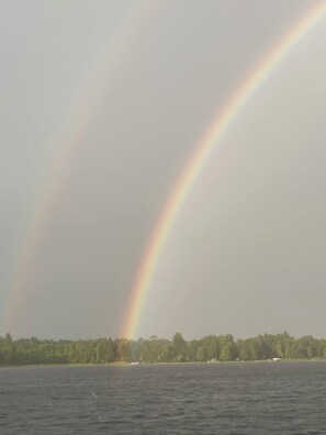 Ein Gewässer mit Regenbogen und bewaldeter Uferlinie.