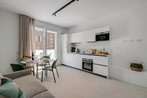 Eine moderne Küche mit weißen Schränken, einer Mikrowelle und einem Backofen. Es gibt einen Essbereich mit Tisch und Stühlen, und ein Sofa im Vordergrund.