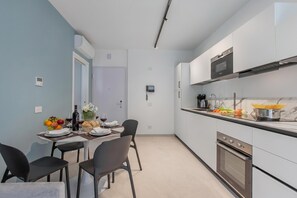 Eine moderne Küche mit weißen Schränken, einem eingebauten Ofen und einer Essecke mit Tisch für zwei Personen.