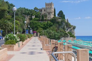 A seaside promenade with a castle on a cliff, a tiled walkway, and beach umbrellas. - Nua Boutique Apartaments 6 Towncentre, Finale Ligure, Italy (Finale Ligure)