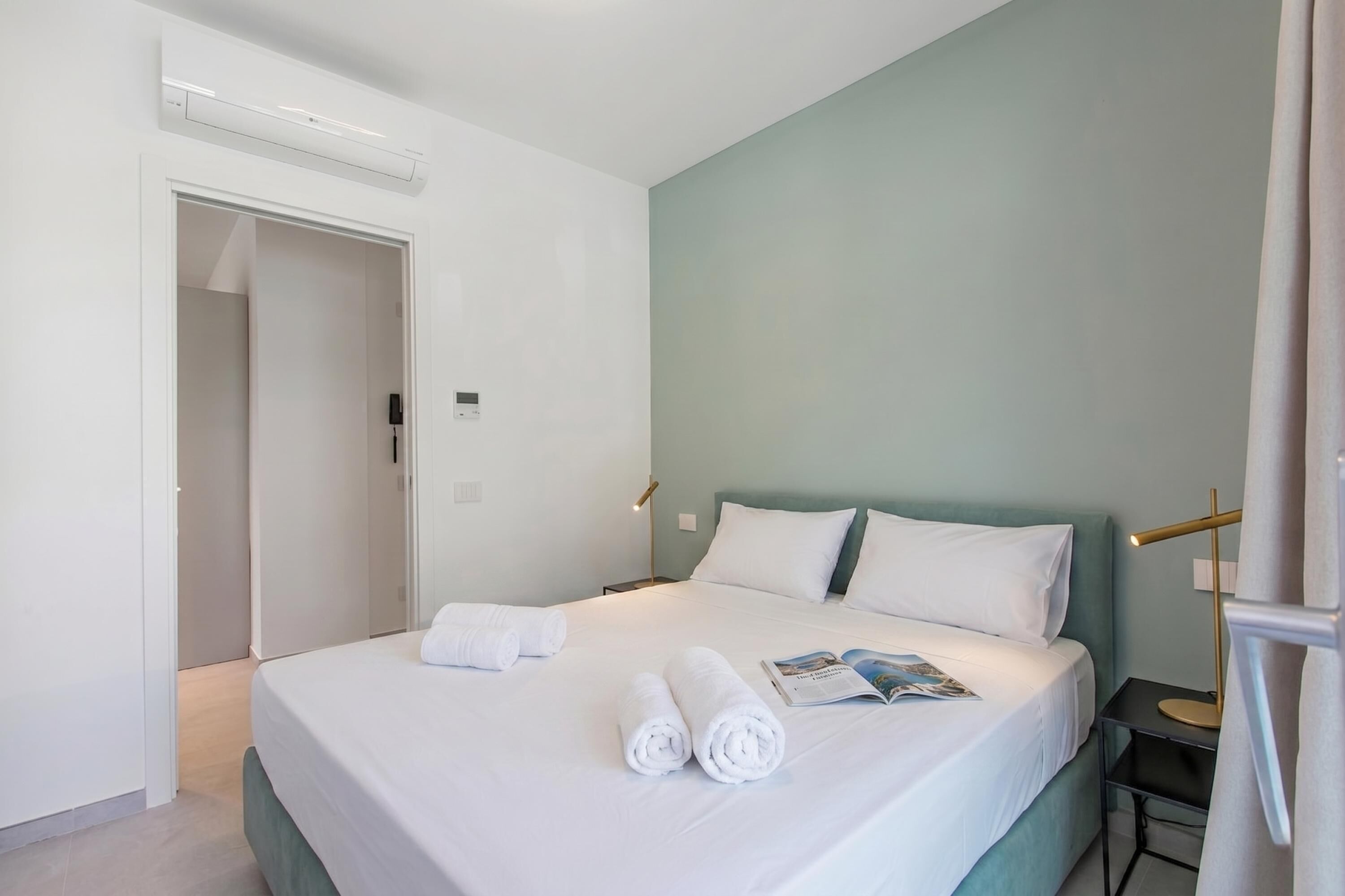 Habitació d'hotel amb un llit, una tauleta de nit, una làmpada i una porta.